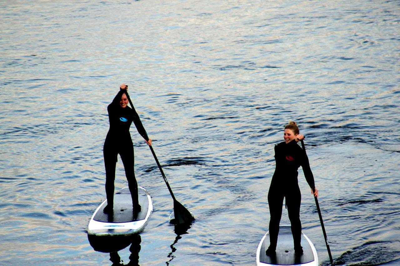 Two stand-up paddlers in wetsuits on the water