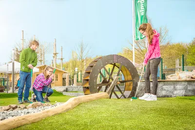 Family playing adventure golf next to a large wooden waterwheel