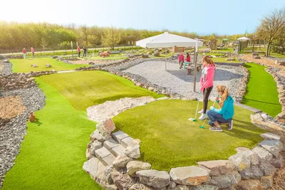 Two girls playing on a long curving adventure golf lane lined with stones