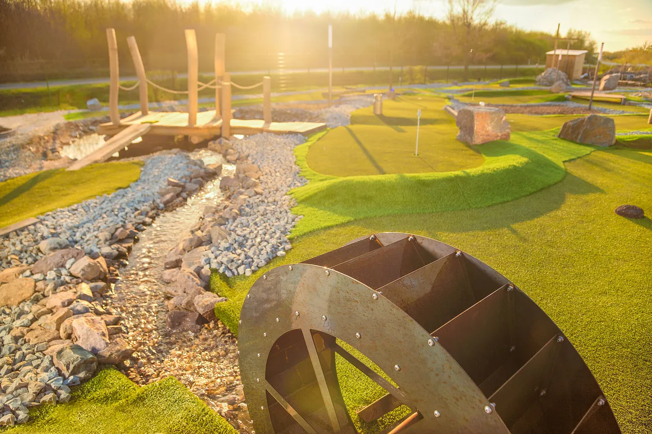 Wooden waterwheel and stream obstacle on a sunlit adventure golf lane
