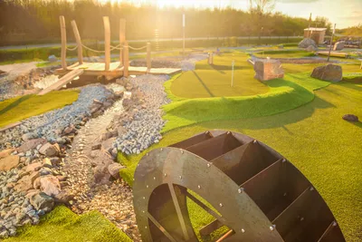 Wooden waterwheel and stream obstacle on a sunlit adventure golf lane