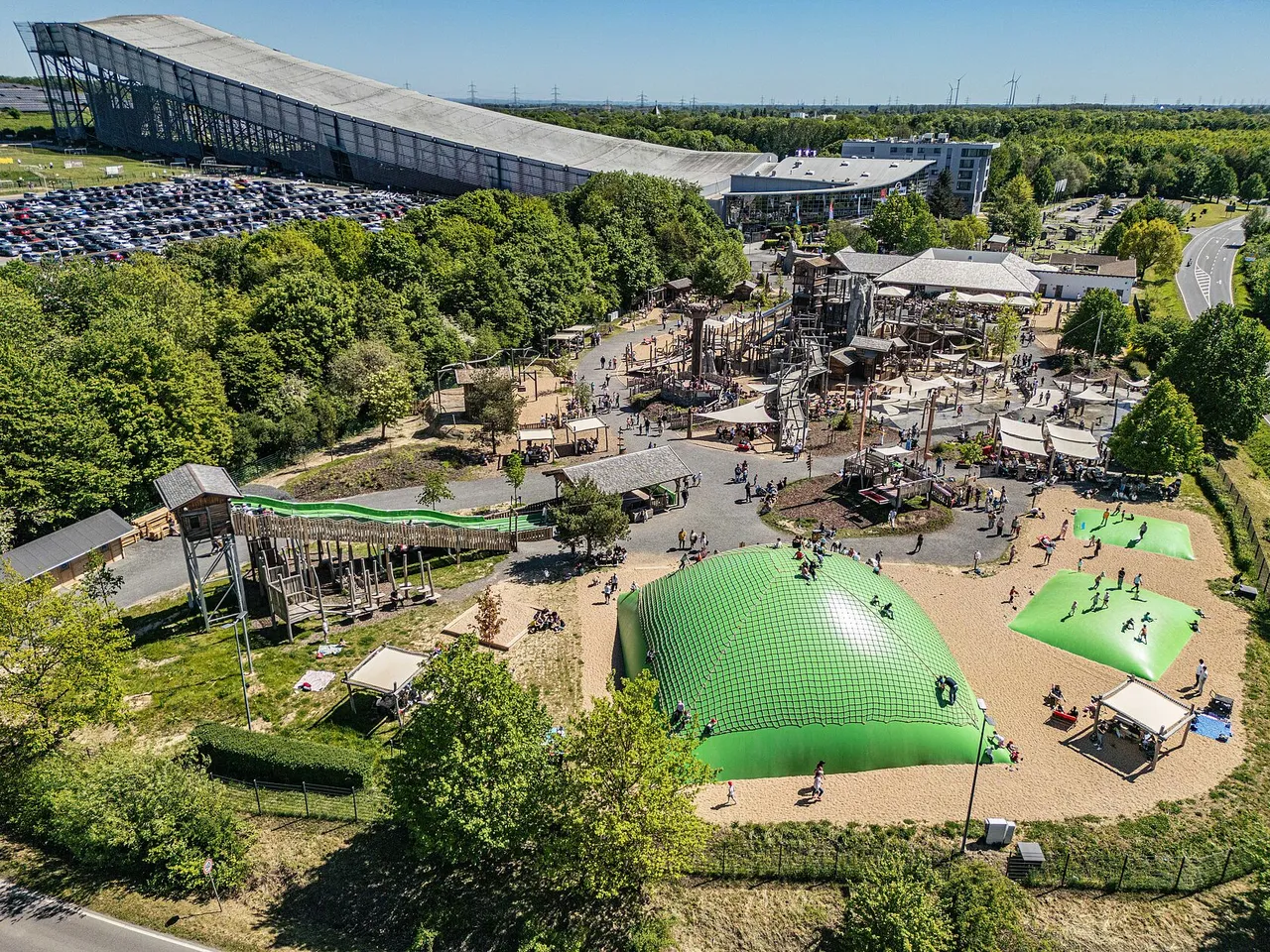 Aerial view of a large adventure playground with climbing towers and giant green bouncy cushions