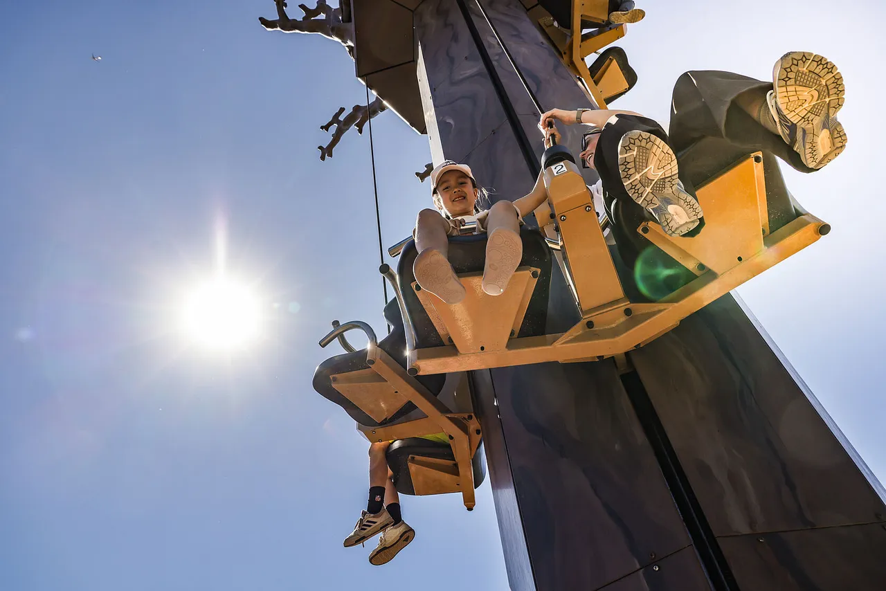 Children riding two-seater gondolas up a tall wooden tower