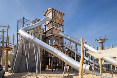 Tall wooden slide tower with long stainless steel tube slides under a blue sky