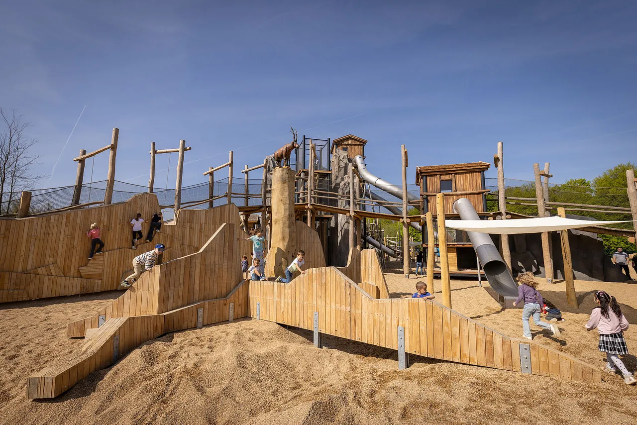 Children playing on wooden climbing structures in a sandy adventure playground