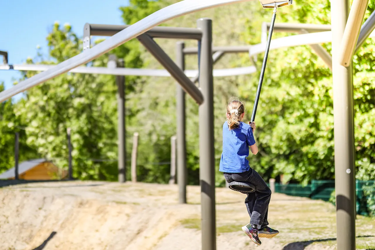 Child riding a mini zip line at an outdoor adventure playground