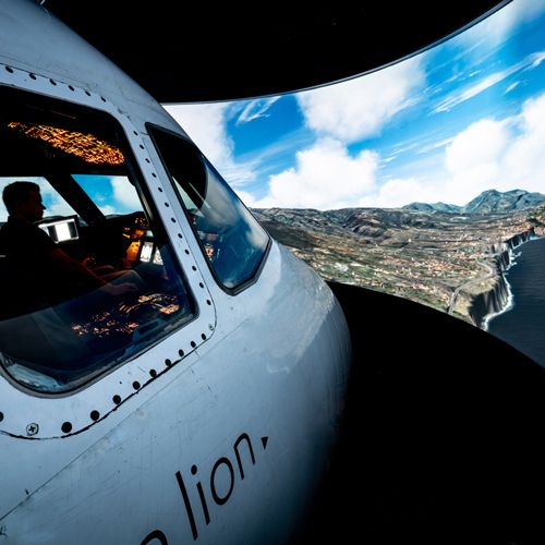 Airbus A320 flight simulator cockpit from outside with a pilot at the controls and a coastal landscape on the projection screen
