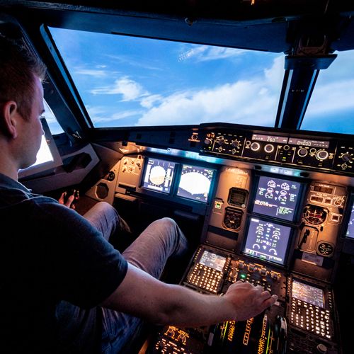 Pilot flying the Airbus A320 flight simulator, hand on the thrust levers, blue sky through the cockpit windows