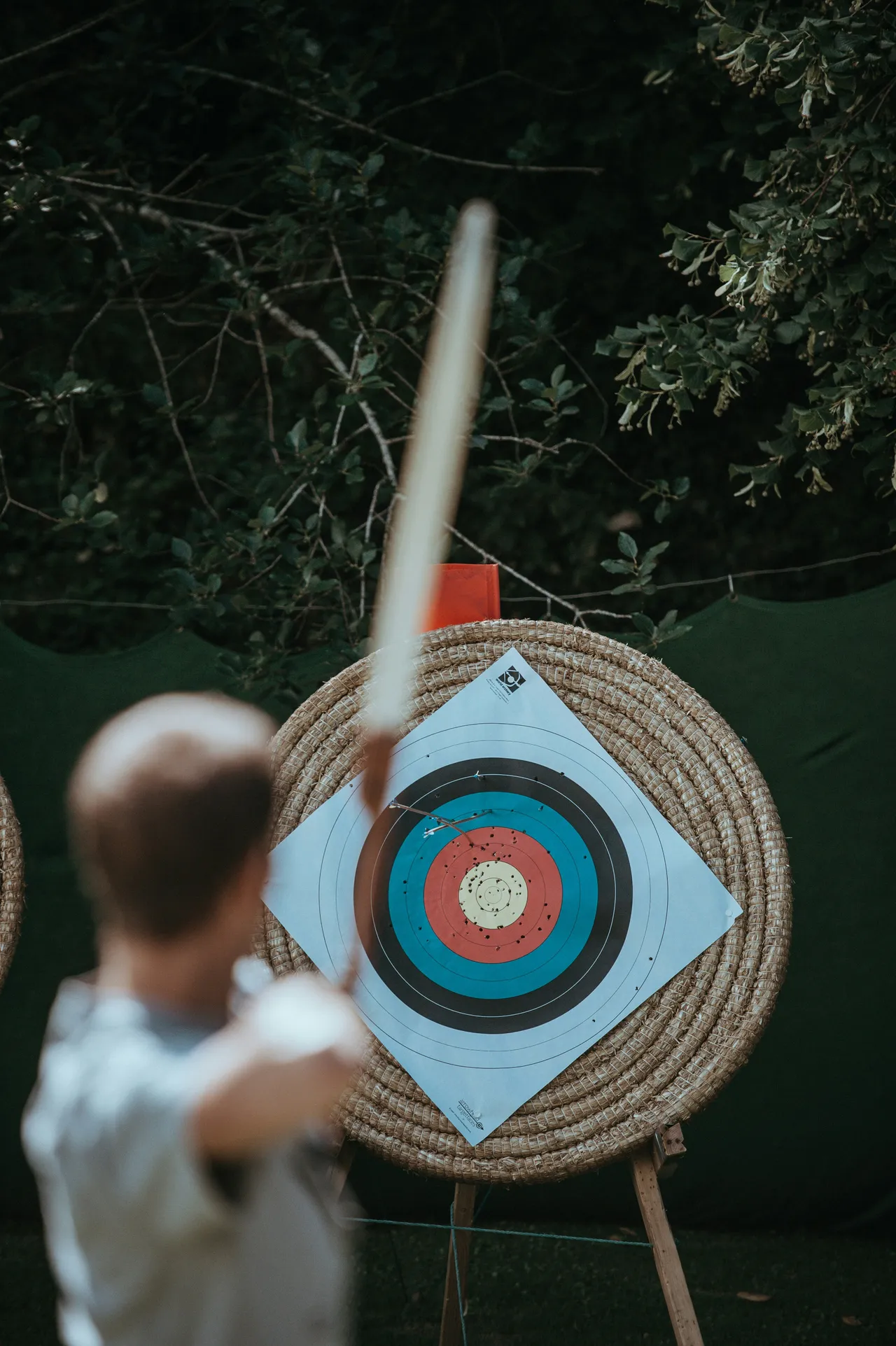 An over-the-shoulder view showing a blurry arrow mid-flight immediately after being released toward a round straw target.