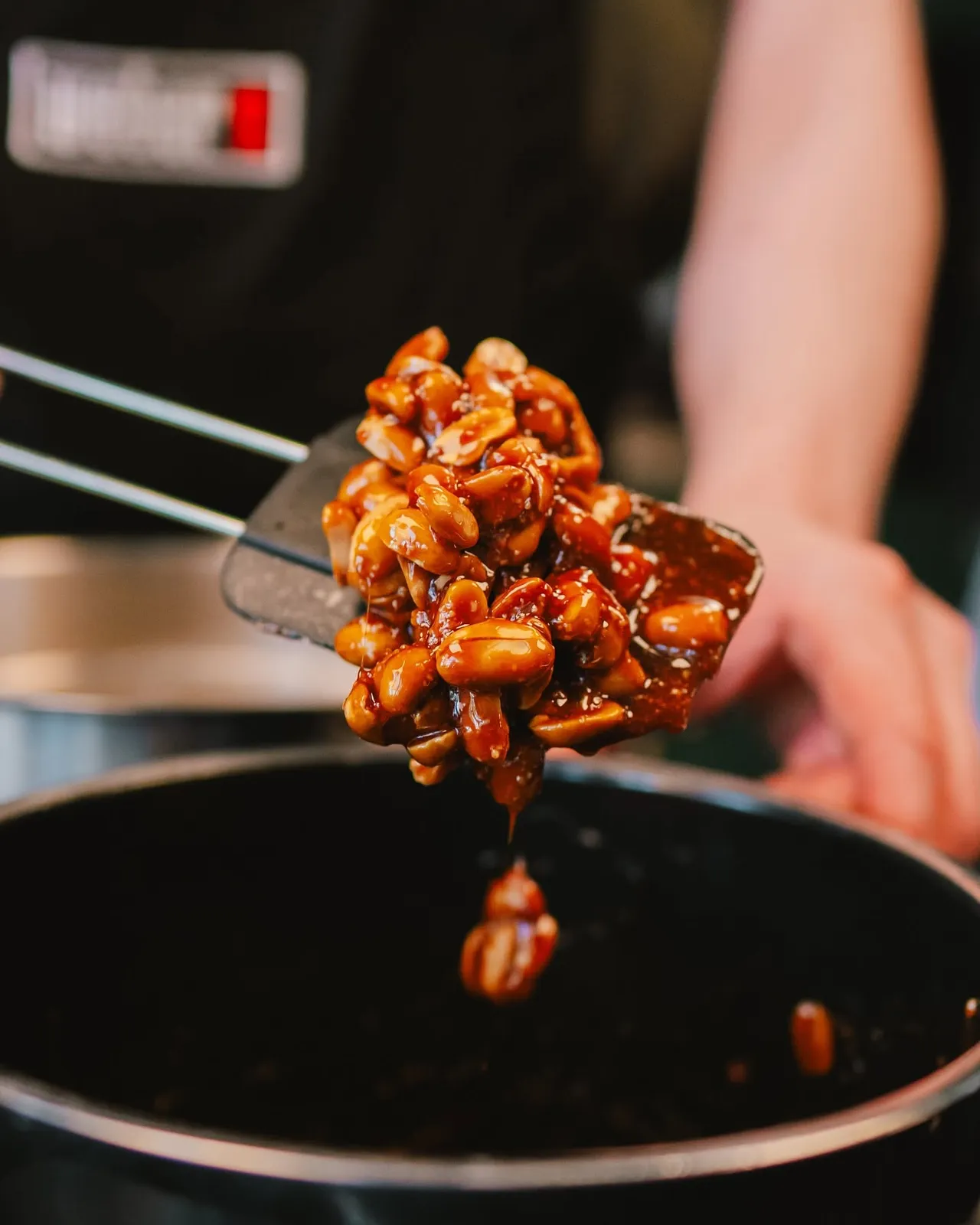 Glazed nuts lifted with tongs from the pan
