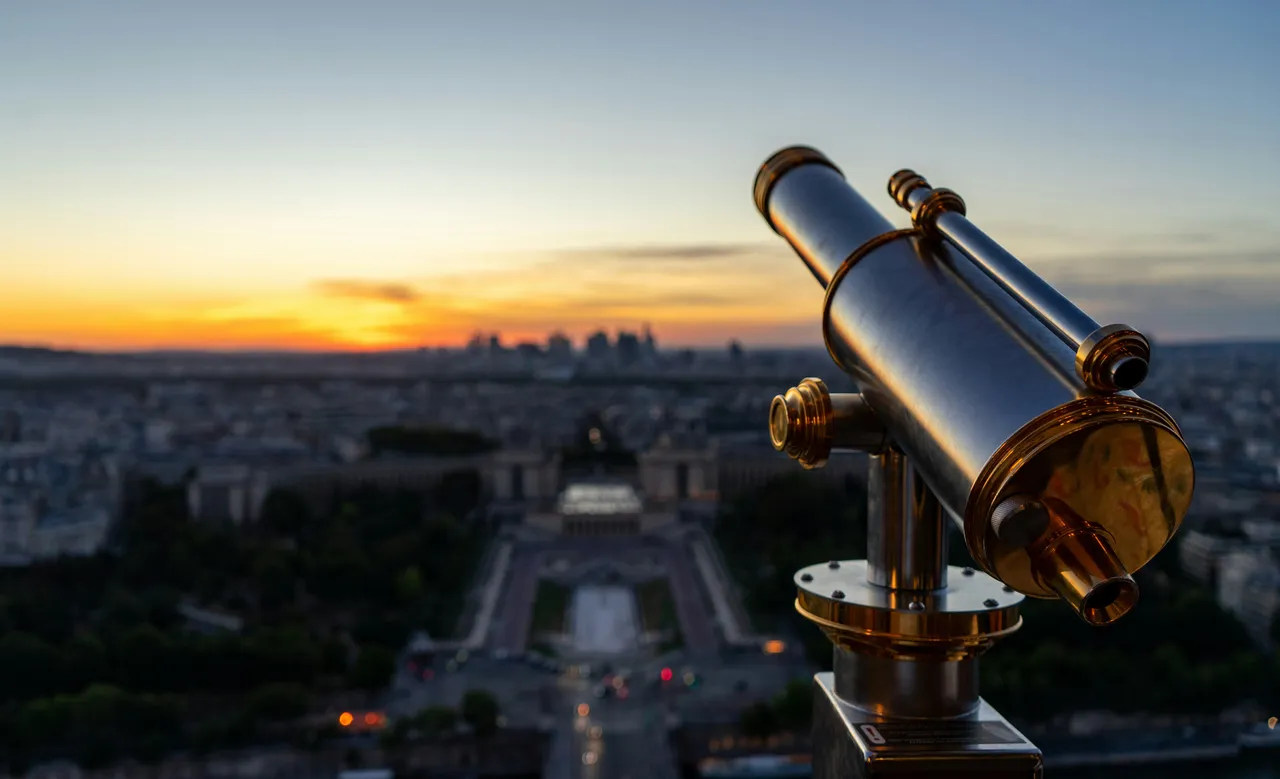 Several large amateur astronomical telescopes are set up on tripods in an open field at dusk, prepared for a night of stargazing under a clear sky.