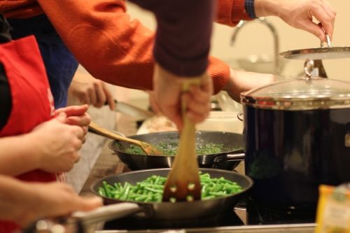 A person stirring green beans and herbs in pans on the stove