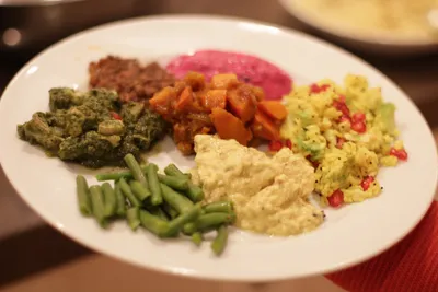 Plate with oriental vegetarian dishes such as green beans, hummus, beetroot dip and rice with pomegranate