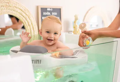 Baby smiling and waving while floating in a baby spa ring, reaching for a rubber duck toy