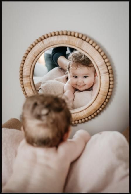 Baby looking curiously at their own smiling reflection in a round mirror during a massage session