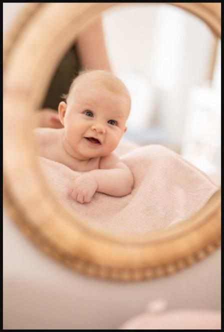 Close-up of a baby lying on a soft blanket, smiling reflection visible in a round mirror