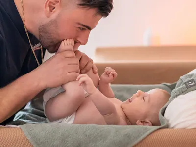 Man kissing the feet of a smiling baby lying on a green towel.