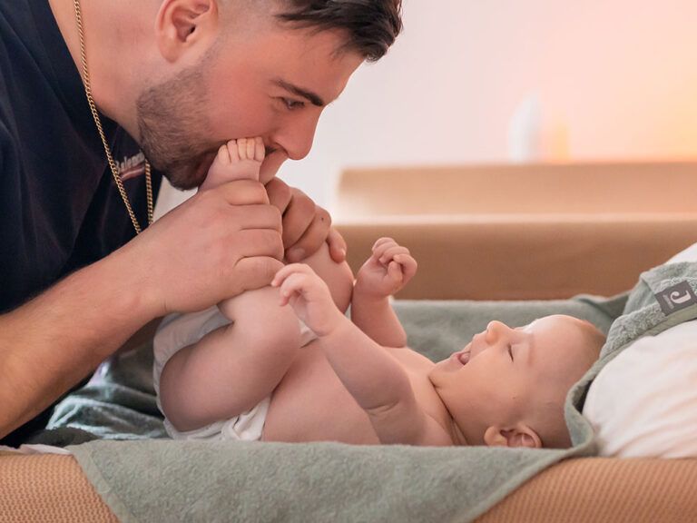 Man kissing the feet of a smiling baby lying on a green towel.