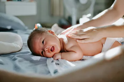 Newborn baby lying on a changing table smiling while a caregiver's hands gently massage its back.