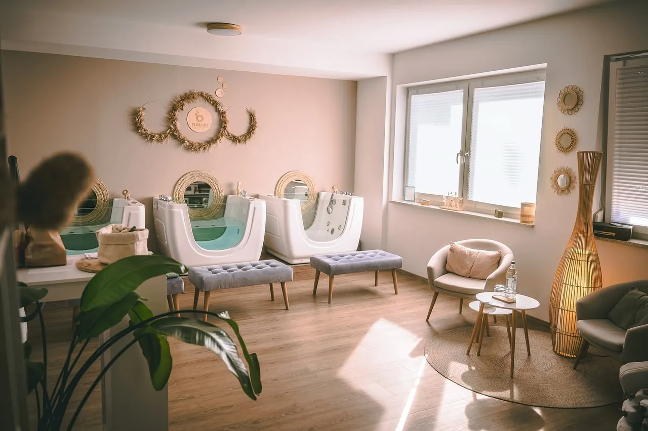 Baby spa treatment room with two flotation tubs, cushioned benches, an armchair, and a woven floor lamp.