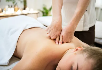 Close-up of a therapist's hands performing a massage on an adult's upper back.