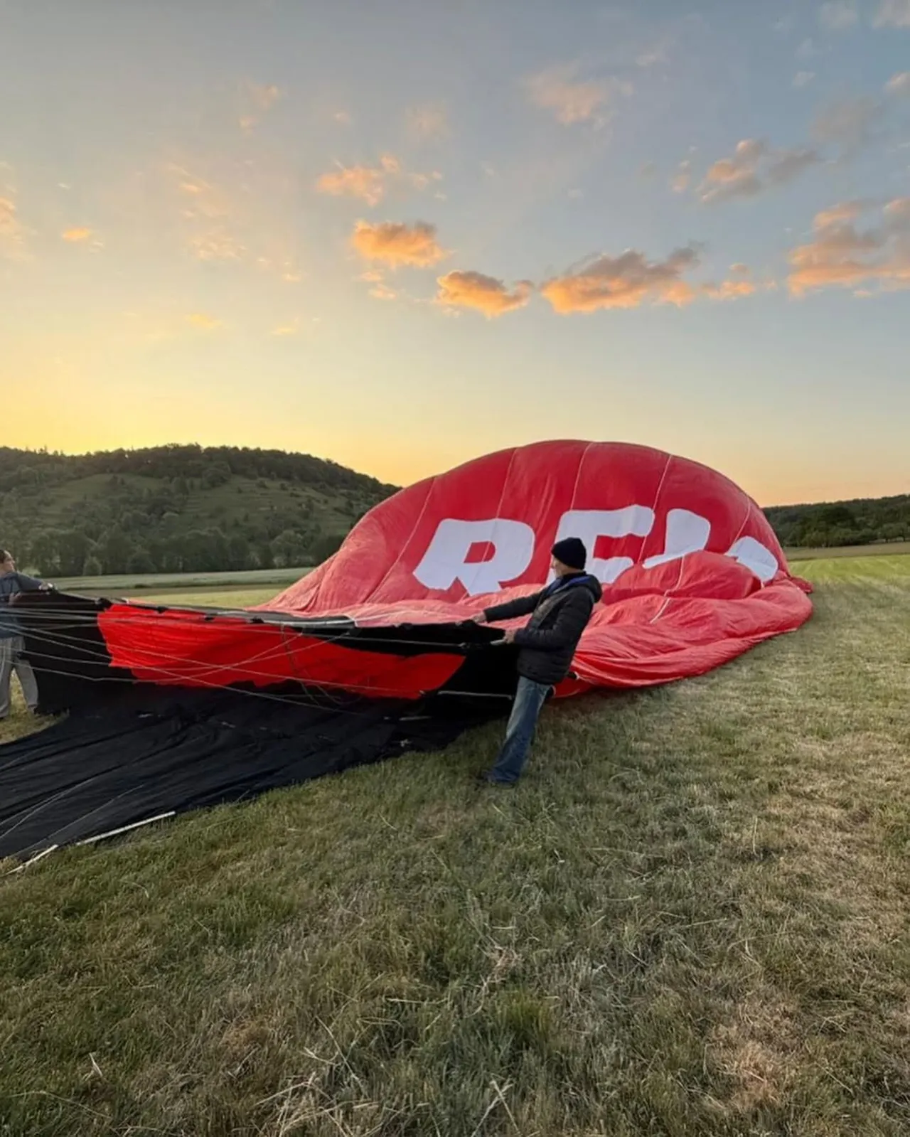 Crew member spreading out the balloon envelope on a meadow at dawn