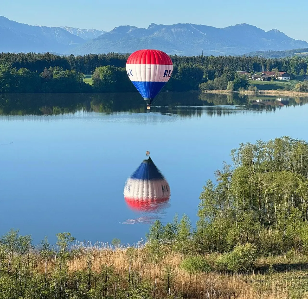 Hot air balloon reflected in a calm lake with mountains in the background