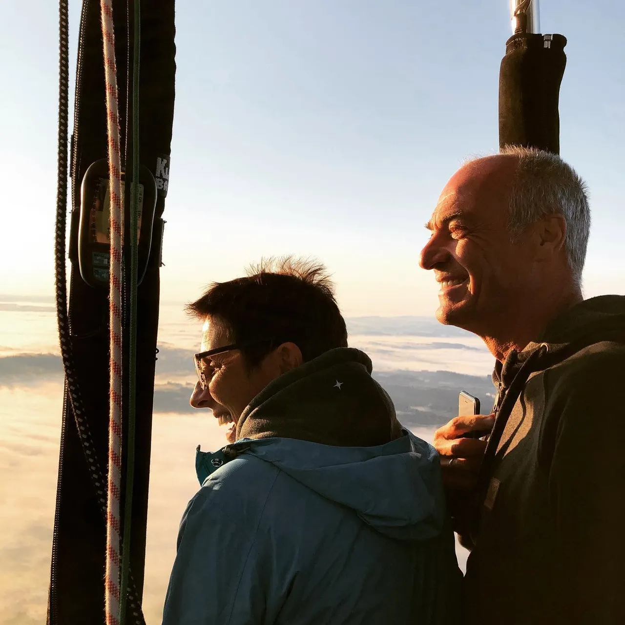 Two passengers in the balloon basket enjoying the view above the morning mist