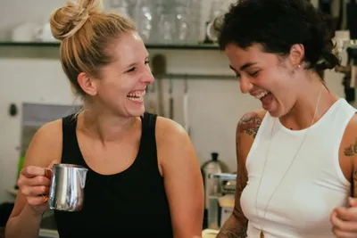 Two women laughing while preparing coffee specialities