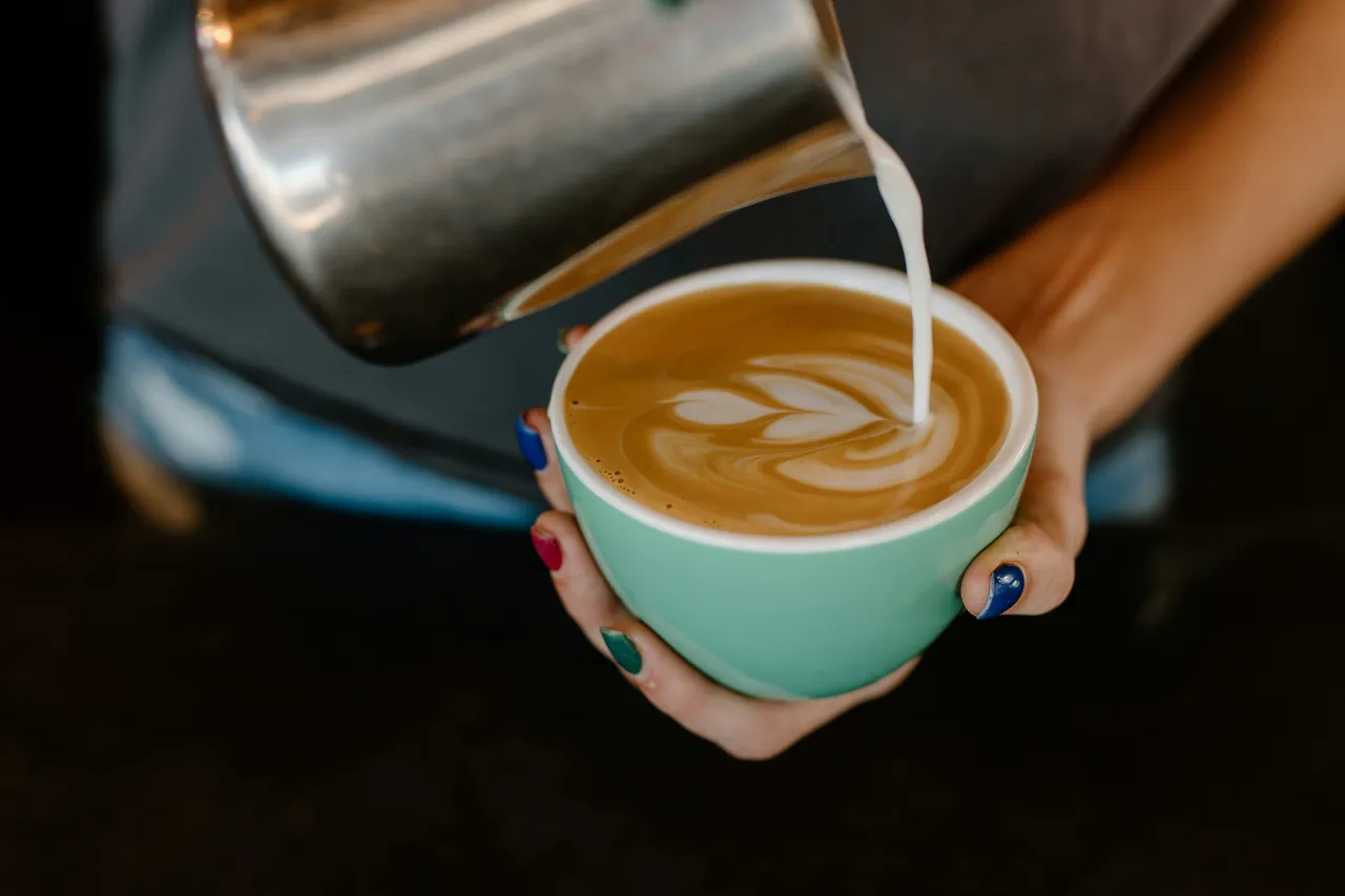 Barista pouring steamed milk into a mint-green coffee cup to create latte art with leaf pattern design.