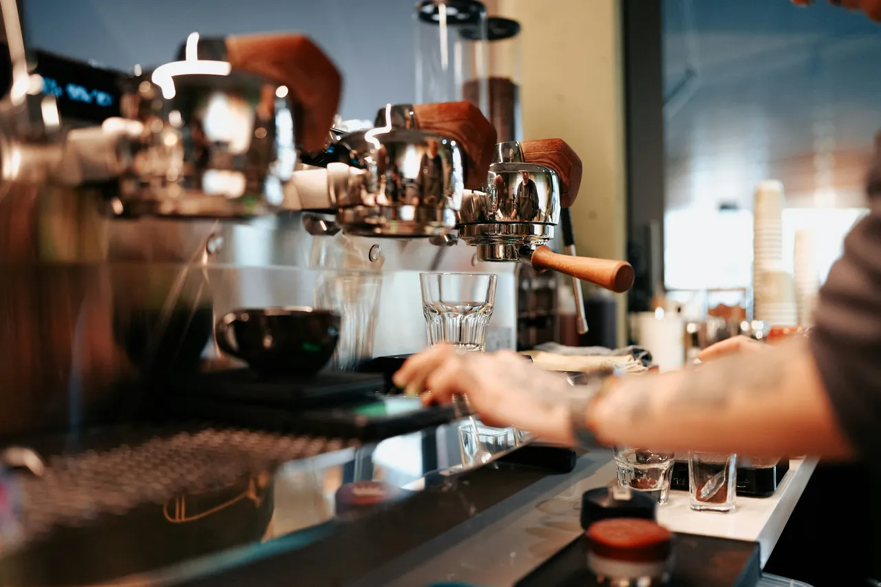 Multiple baristas working along a professional espresso machine bar with empty glasses positioned in front, ready for drinks service.
