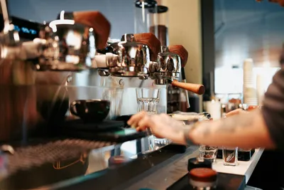 Multiple baristas working along a professional espresso machine bar with empty glasses positioned in front, ready for drinks service.