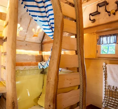 Wooden sleeping area with ladder, striped curtain and crown-shaped cutouts in a treehouse