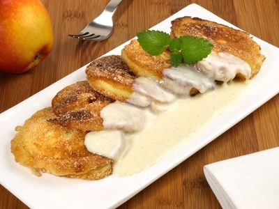 Apple fritters with cinnamon sugar and vanilla sauce on a white plate