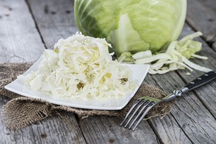 Plate of sauerkraut next to a fresh white cabbage on a rustic table