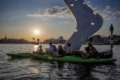 Group paddling past the Molecule Man sculpture on the Spree in Berlin at sunset