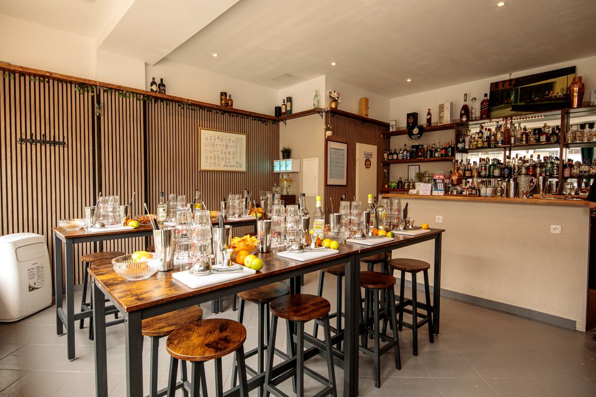 Bar room set up for a beginners cocktail making course, with high tables, tasting glasses, and a well-stocked bar shelf in the background.