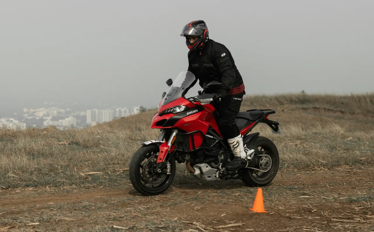 An enduro rider in full protective gear and helmet navigates a rugged dirt trail through a dense forest.