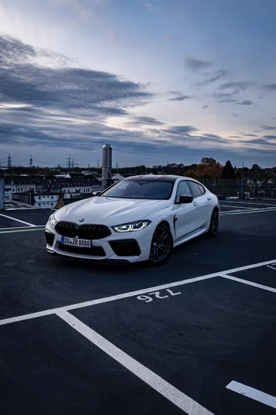 White BMW M8 Competition xDrive parked on a rooftop car park at dusk, seen from the front three-quarter angle