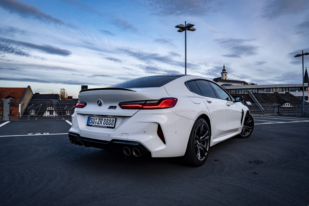 Rear three-quarter view of a white BMW M8 Competition xDrive with quad exhaust on a rooftop car park