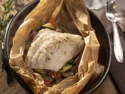 White fish fillet with vegetables cooked in parchment paper in a dark dish