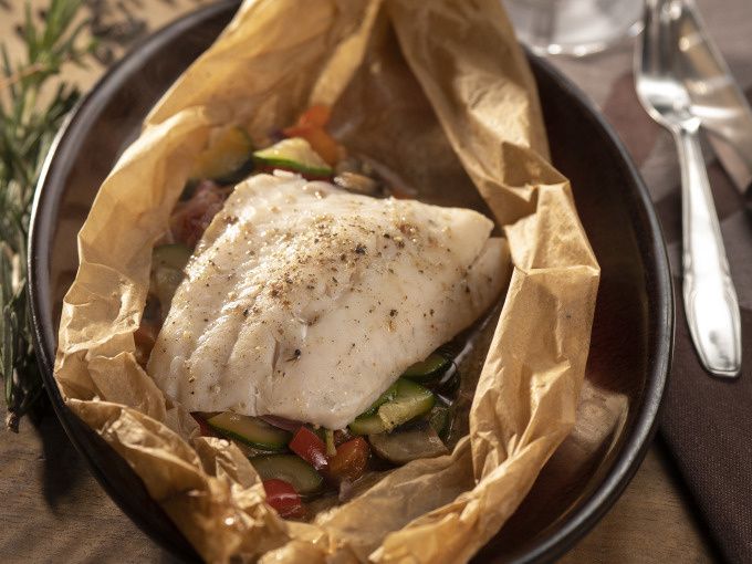 White fish fillet with vegetables cooked in parchment paper in a dark dish