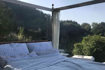 Bed with patterned pillows inside a transparent tent looking out onto green wooded hills