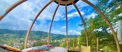 View from the bed inside a transparent bubble tent with wooden frame over the green Odenwald valley and village