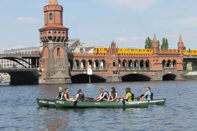 Canoe with paddlers in front of Oberbaum Bridge in Berlin as a yellow metro train crosses
