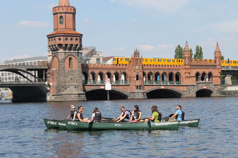 Canoe with paddlers in front of Oberbaum Bridge in Berlin as a yellow metro train crosses