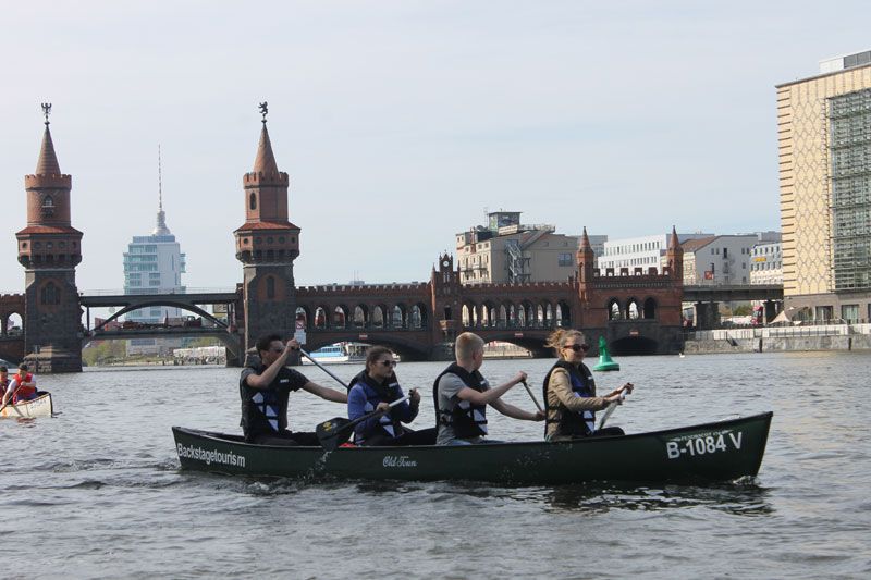 Four paddlers in a canoe on the Spree with Oberbaum Bridge and the Berlin TV Tower behind