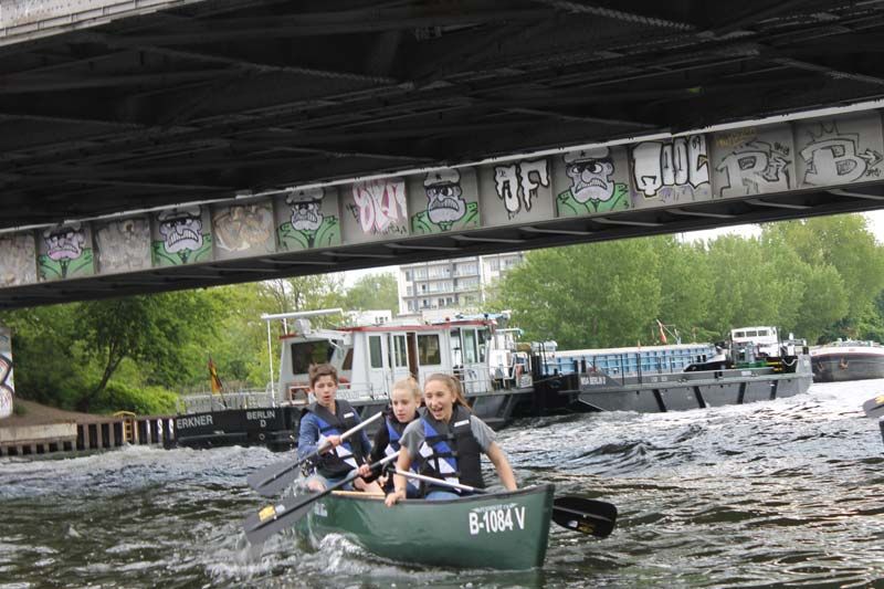 Paddlers in a canoe passing under a graffiti-covered railway bridge on the Spree in Berlin