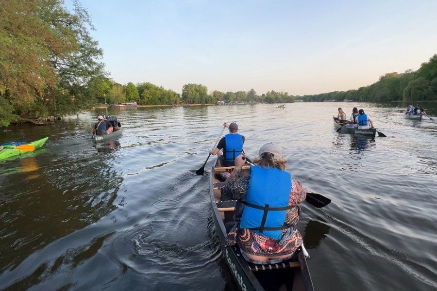 View from a canoe of several boats paddling down the tree-lined Spree river in Berlin