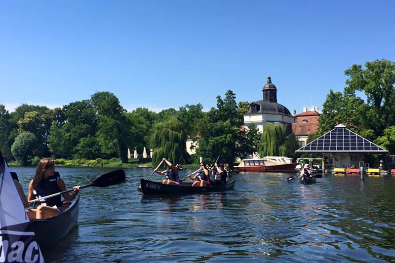 Canoes with paddlers on the water in front of the baroque Köpenick Palace in Berlin